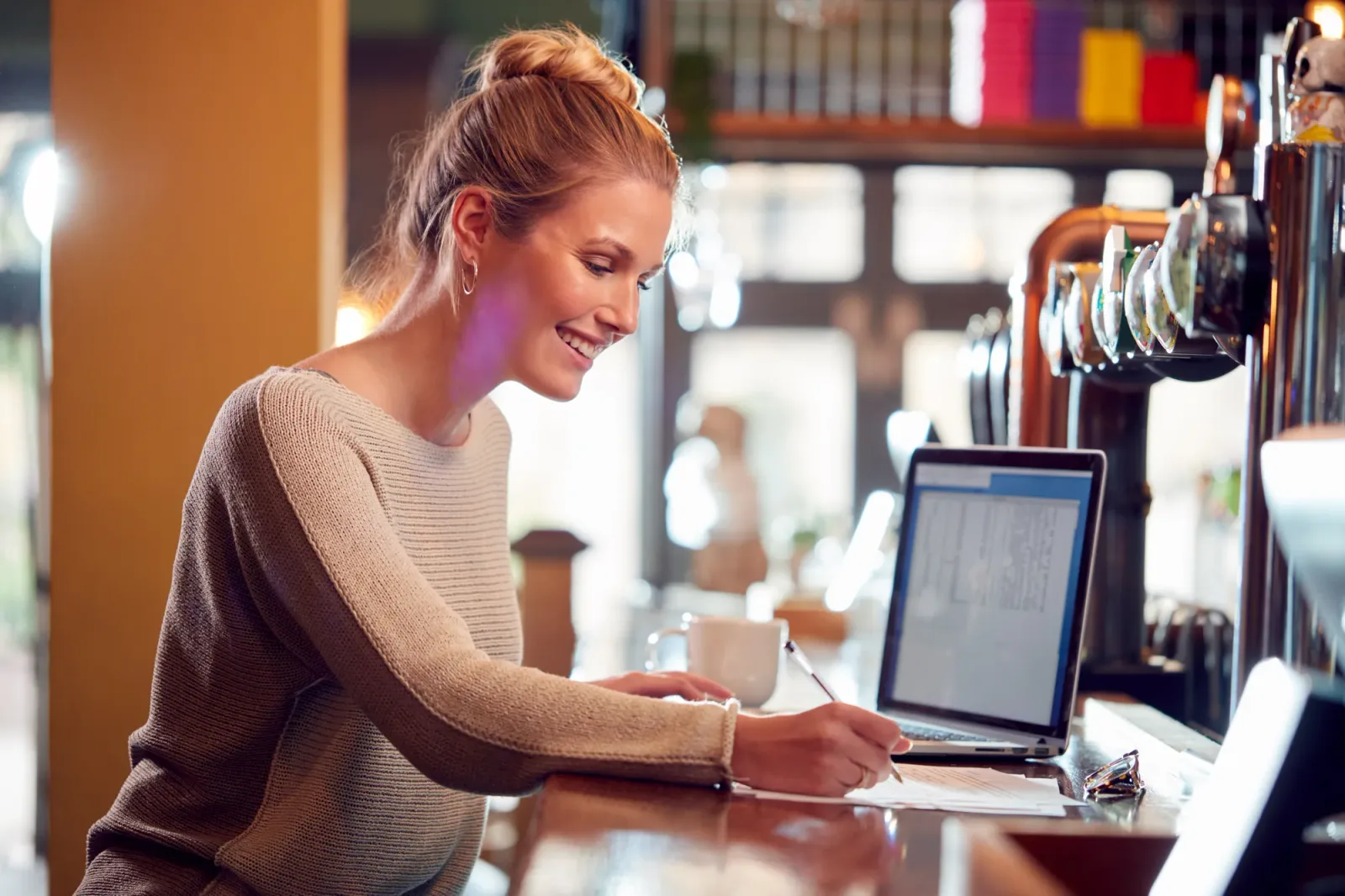 A pub manager planning at the bar with a laptop and notes